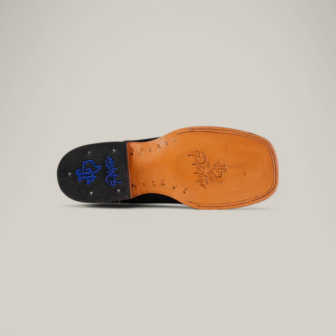 The image features the sole of the Black Suede - Platinum - Square Toe cowboy boot. It has a tan square toe with metal studs and embossed logos: one in blue reading Rios of Mercedes, and a stylized signature, both perfectly complementing platinum accents.