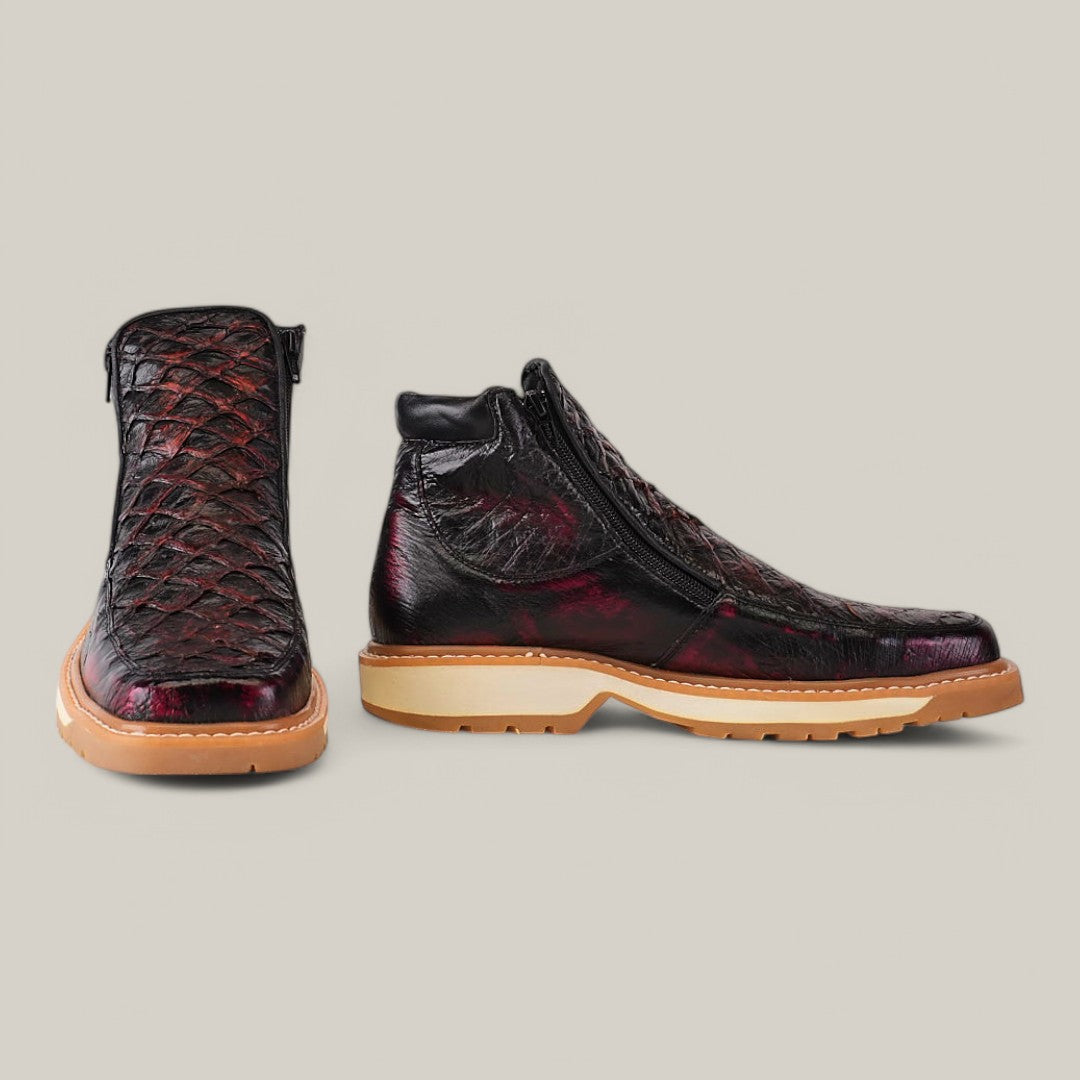 The Exotic Pirarucu Fish - Black Cherry Ankle Boots are made from luxurious Pirarucu leather with red and black cherry textures, featuring side zippers and tan rubber soles. One boot stands upright showing its sleek design, while the other lies on its side, highlighting the zipper and sole.