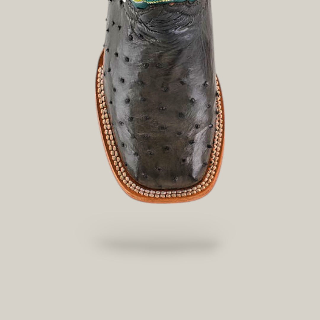 A close-up of the Exotic Full Quilt Ostrich Gray Kids Boot features a square toe, intricate stitching, gray ostrich leather, and a tan sole, showcasing western style against a simple light background.