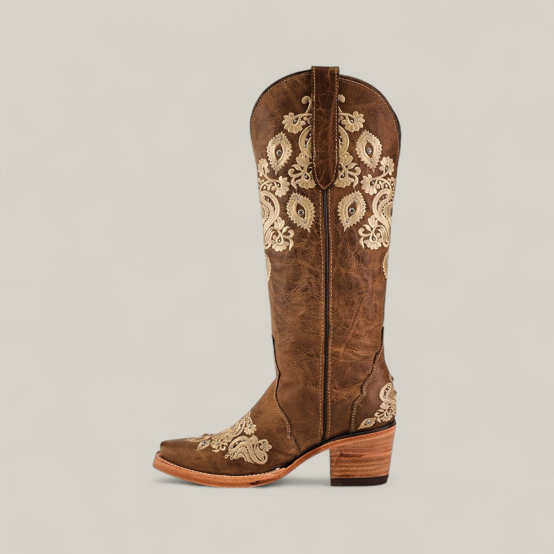 The Roxanne Crystals Tabaco is a tall shaft womens luxury brown leather boot with a medium wooden heel and beige paisley embroidery, featuring a snip toe for an elegant touch. Displayed on a light neutral background.