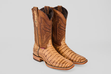 A pair of Exotic Caiman Belly - Antique - Square Toe boots with a brown, crocodile-like textured foot and decorative stitching on the shaft, shown against a plain gray background.