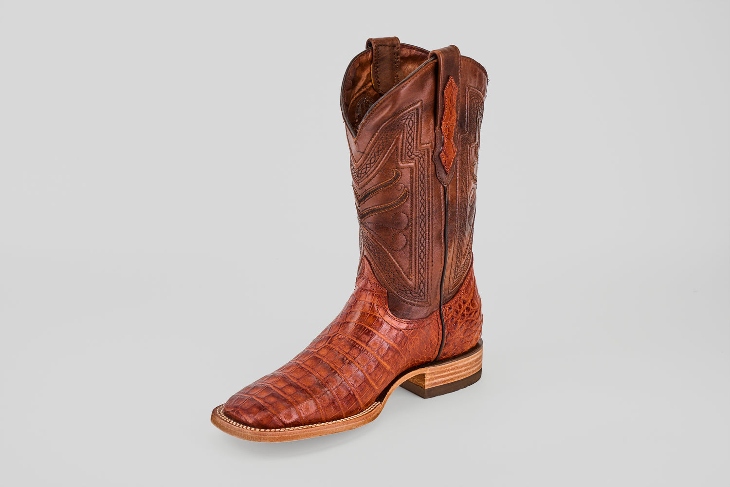 A single Exotic Caiman Belly - Brandy - Square Toe boot featuring detailed stitching and a textured pattern stands upright on a light gray background.