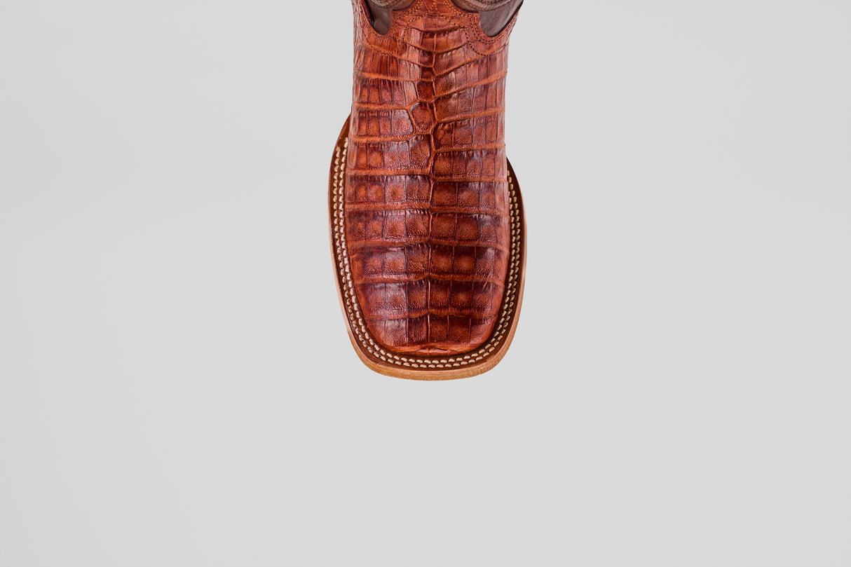 Close-up, top-down view of the Exotic Caiman Belly - Brandy - Square Toe boot, showing its brown, square toe with a textured reptile-patterned leather and white stitching along the edge.