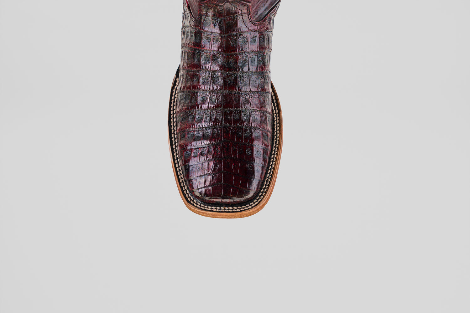 A close-up of the toe of the Exotic Caiman Belly - Black Cherry - Square Toe boot, highlighting its handcrafted crocodile-patterned finish, square shape, and rich detailed stitching—showcasing true luxury.