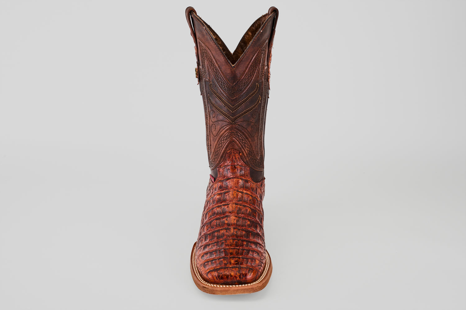 The Exotic Caiman Horn Back - Smoke Cogñac- Square Toe boot features textured caiman leather with decorative stitching, shown from the front against a plain light gray background.
