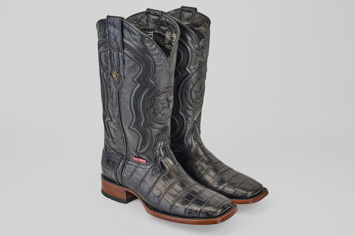 A pair of Exotic Alligator Tail - Black - Square Toe boots, featuring embossed leather, wooden soles, and detailed shaft stitching, displayed on a plain light gray background.
