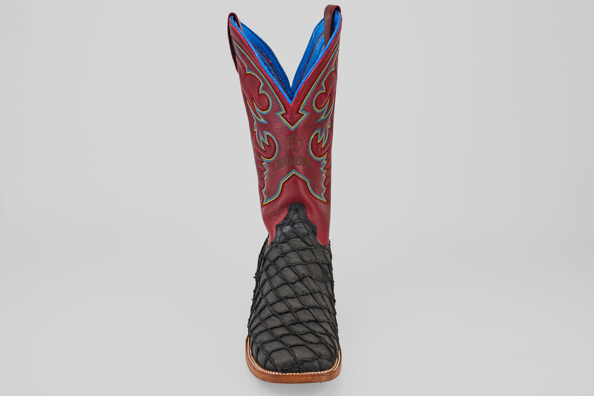 The Dodge - Matte Black - Square Toe boot features a textured black Pirarucu leather foot, square toe, brown sole, and a tall red shaft with decorative stitching and blue lining. Mens luxury boot shown facing forward on a plain background.