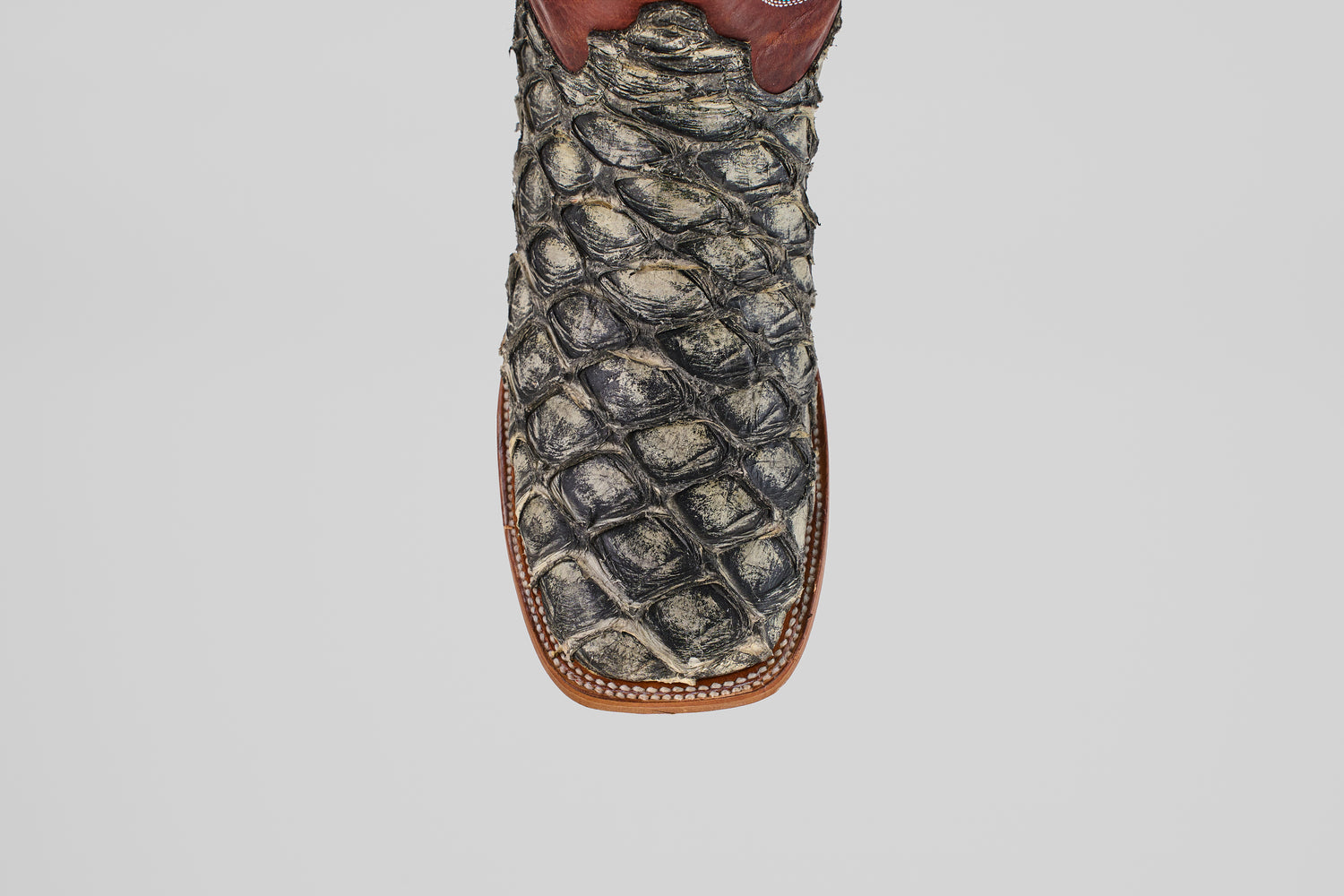 A detailed, top-down view of the Robinson - Newspaper - Square Toe boot highlights its textured Purarucu leather, brown trim, and white stitching—showcasing these distinctive handcrafted boots.