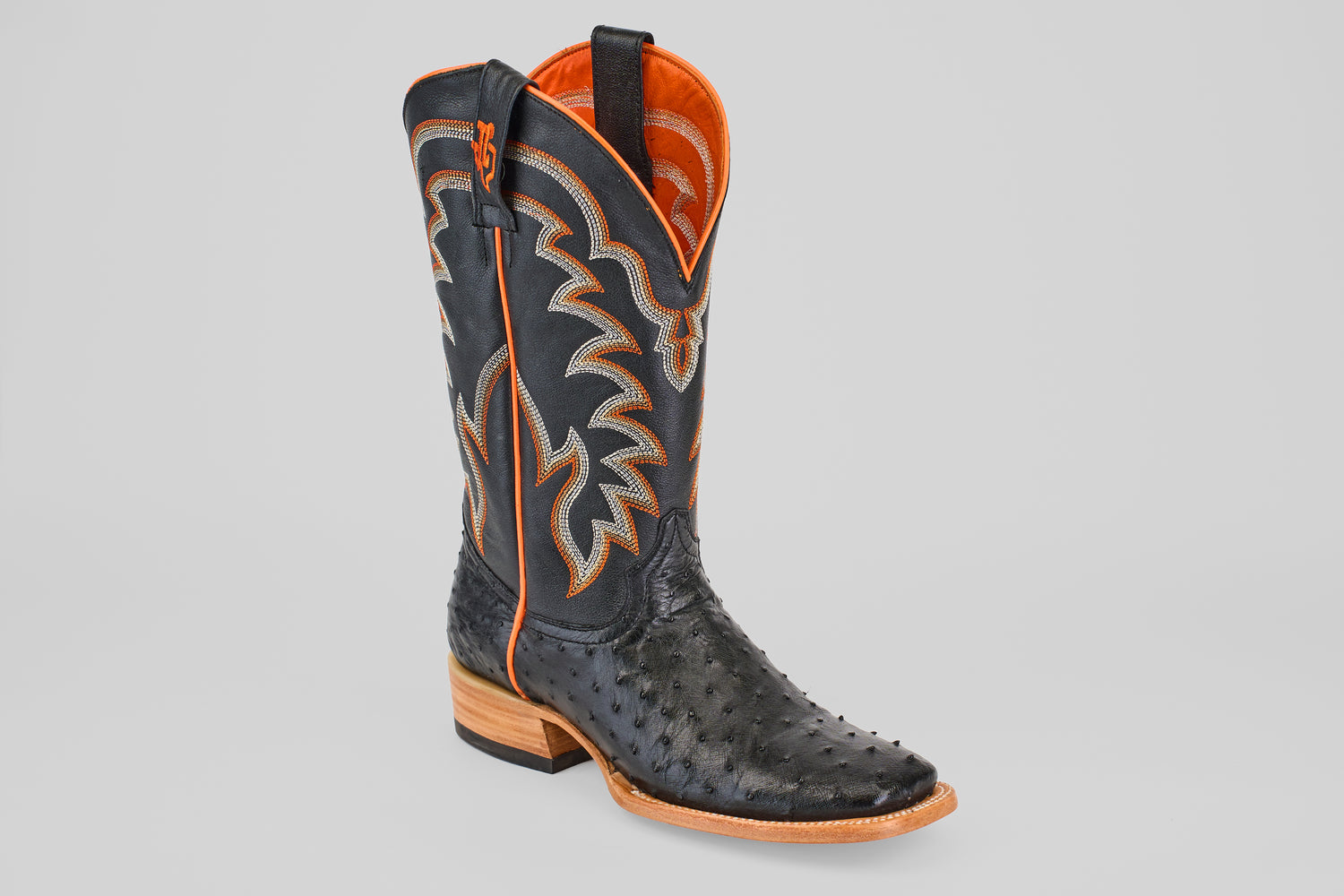 The Steele - Black - Square Toe boot features a black ostrich leather pattern, orange and tan stitching, an orange interior lining, and a light brown wooden heel—luxurious footwear for those seeking standout style.