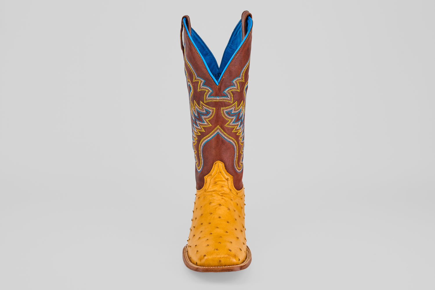 The Ransom - Buttercup - Square Toe Boot features a yellow exotic full quill ostrich leather foot and a brown shaft with blue and yellow stitching, shown on a plain light gray background.