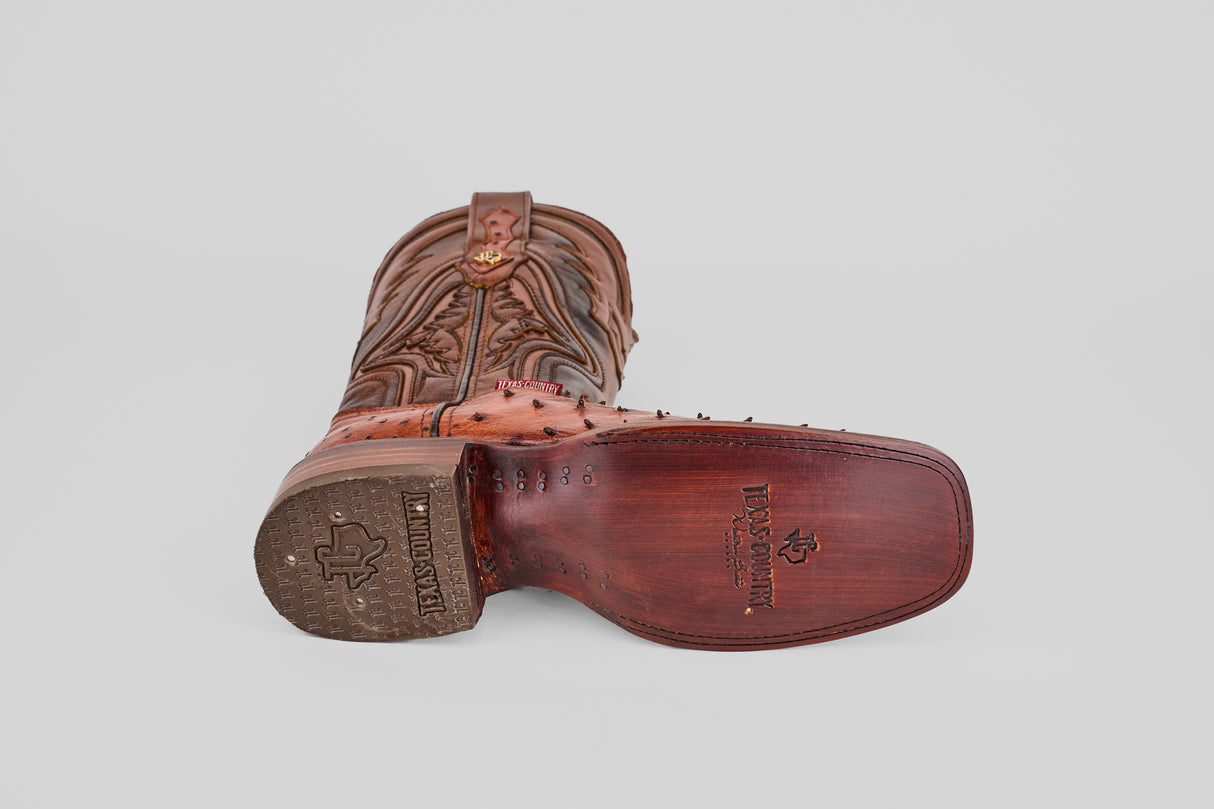 The Exotic Ostrich - Brandy - Rodeo Toe boot features detailed top stitching and displays its branded text and logo on a polished wooden sole, all crafted from genuine ostrich leather in a rich brown hue.