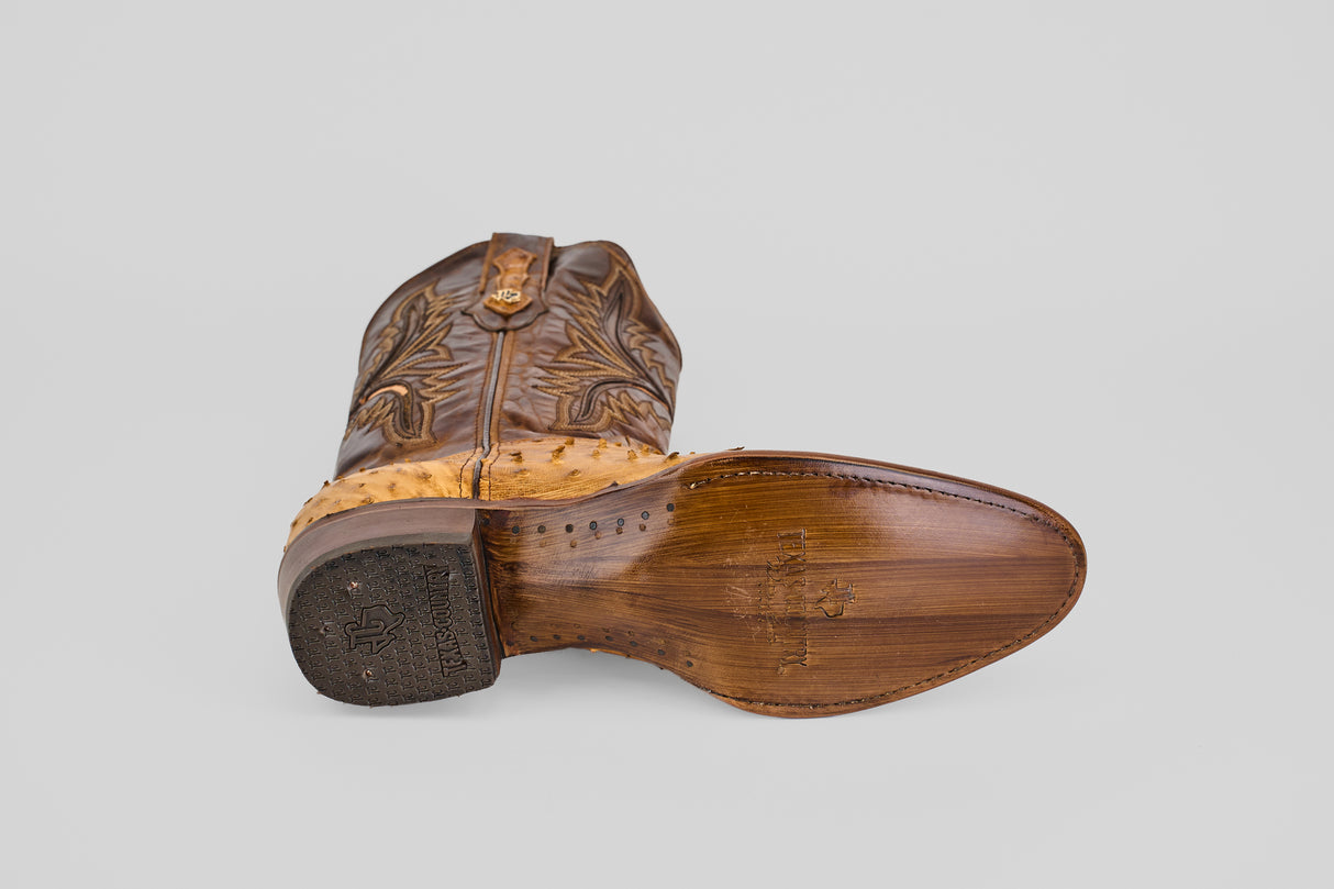 The Exotic Full Quilt Ostrich - Paja - Round Toe boot, in brown leather, features a round toe, wooden-textured sole, stitched edges, and intricate decorative stitching on the upper.