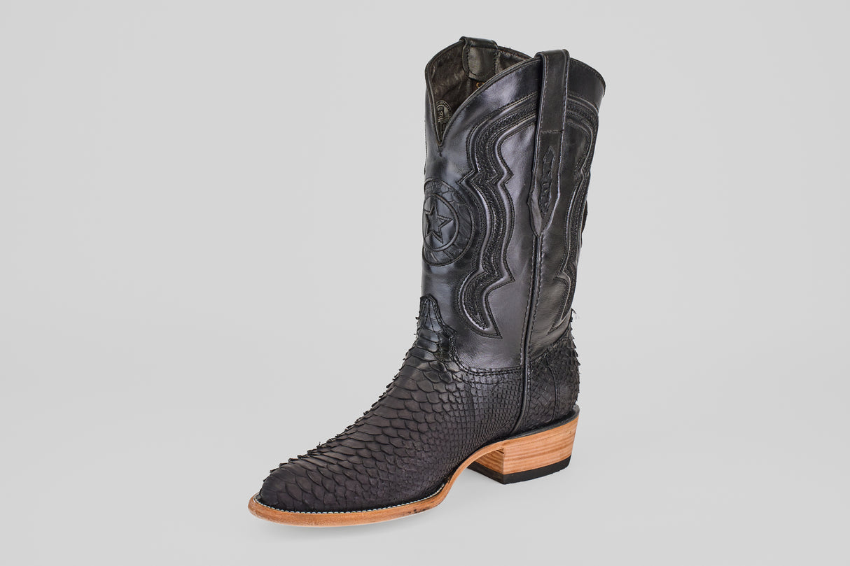 The Tanner – Matte Black – Roper Toe is a single matte black cowboy boot with detailed stitching on the leather upper, textured scales on the lower part, and a light brown stacked heel and sole, shown against a plain light background.