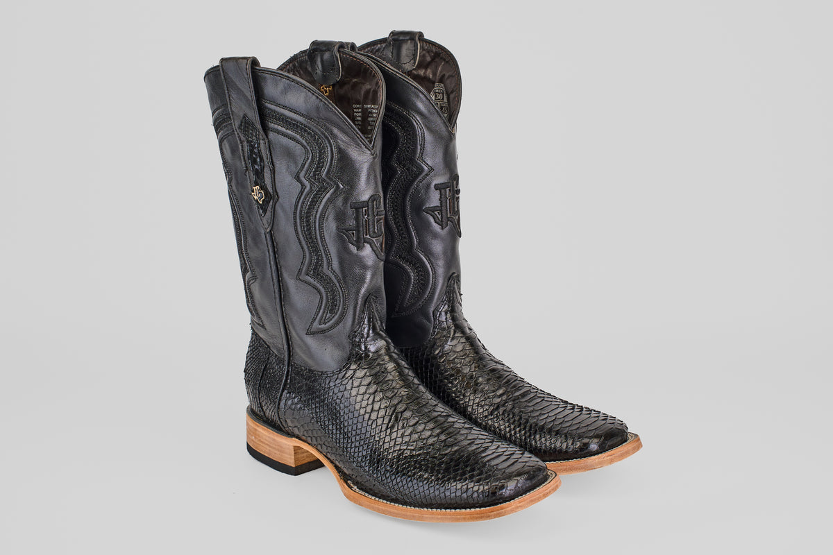 The Tanner - Black - Square Toe boots feature black leather with a Python Negro pattern, wooden soles, and decorative stitching on the shafts, shown against a plain light gray background.