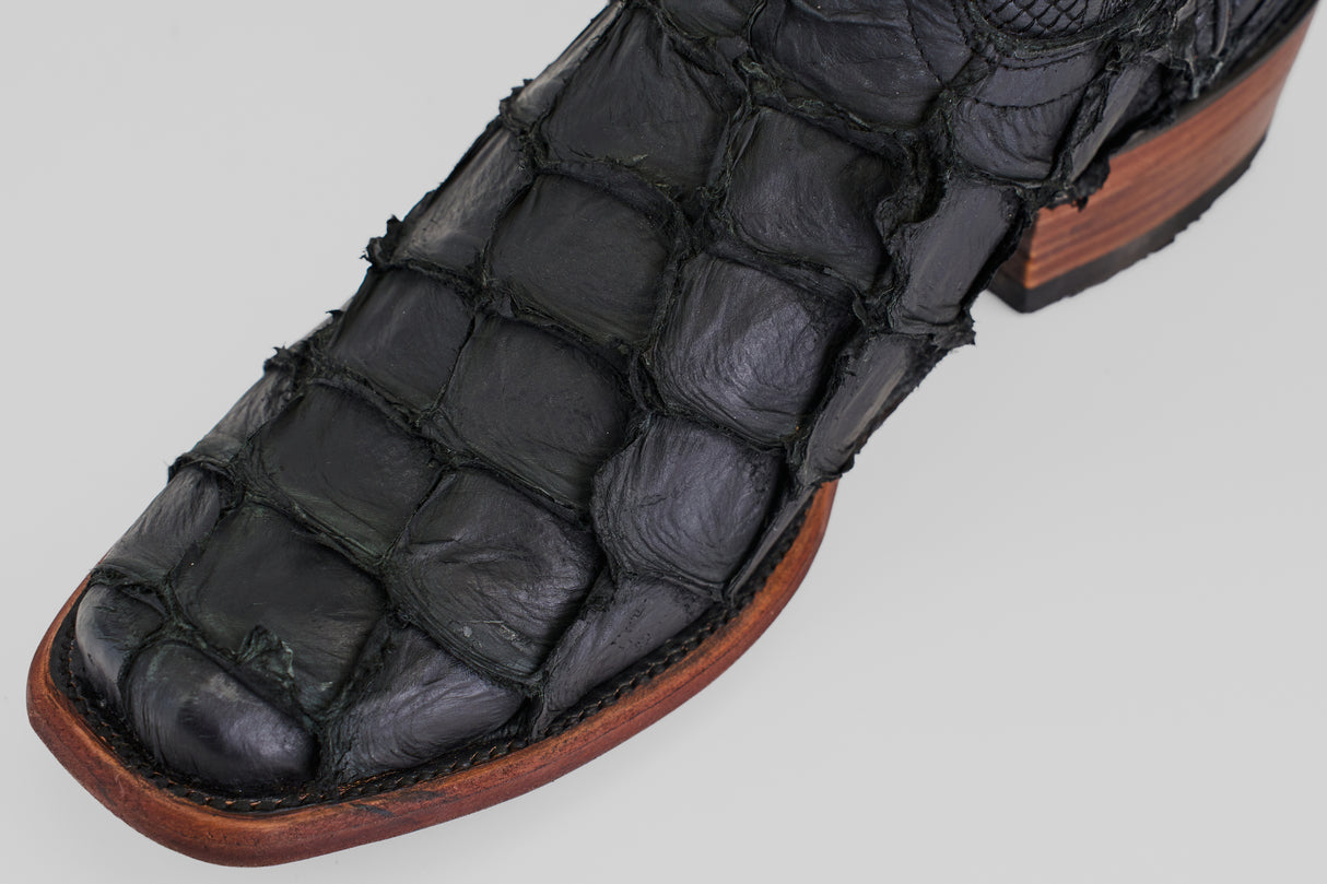 Close-up of the toe and side of the Conor - Matte Black - Narrow Square Toe cowboy boot, crafted from textured alligator or crocodile leather with detailed stitching and a brown wooden sole.