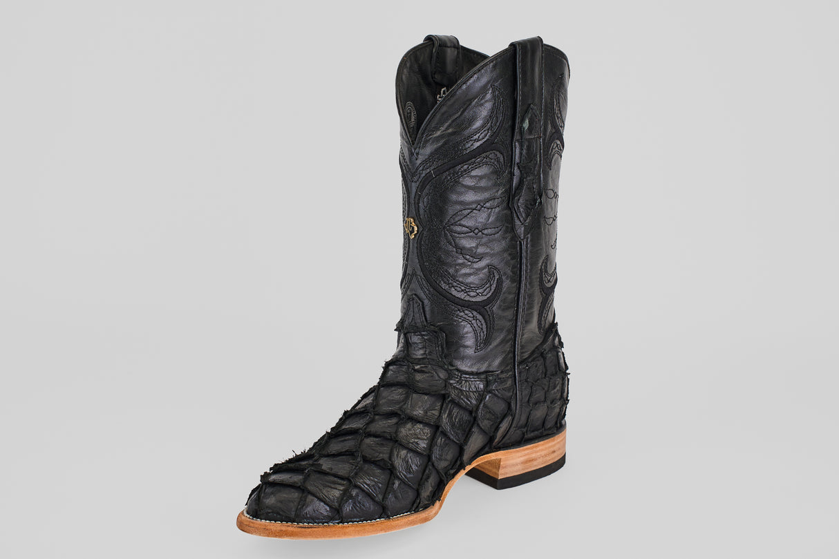 The Conor - Matte Black - Roper Toe is a single black western boot made from pirarucu fish leather, featuring a matte textured surface, brown wooden sole, detailed stitching, and raised designs on the upper.