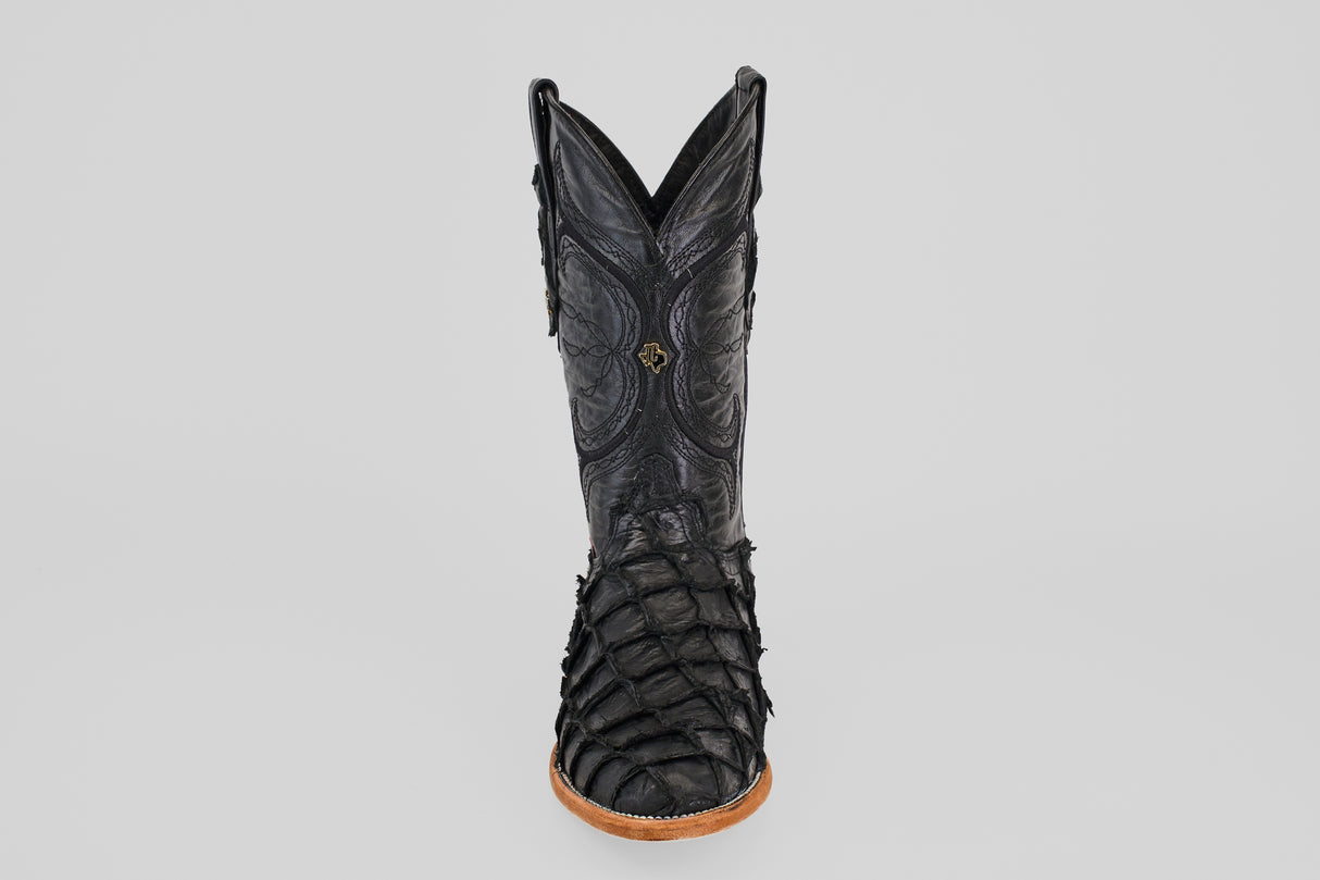 A single Conor - Matte Black - Roper Toe boot made from black pirarucu fish leather, featuring detailed stitching and textured scales on the lower section. Viewed from the front against a plain light gray background with a tan sole.