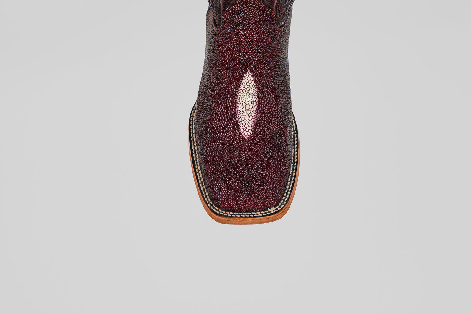 A close-up, top view of the Ranger – Wine – Square Toe boot shows textured, shiny maroon stingray leather and light brown welt stitching around the sole, set against a plain gray background.