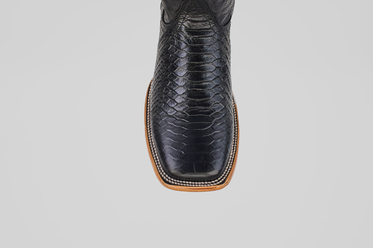 Close-up top view of the Python Black - Embossed Leather - Square Toe (E425) cowboy boot, featuring a shiny textured snakeskin pattern and light brown sole, stylishly displayed against a plain white background.