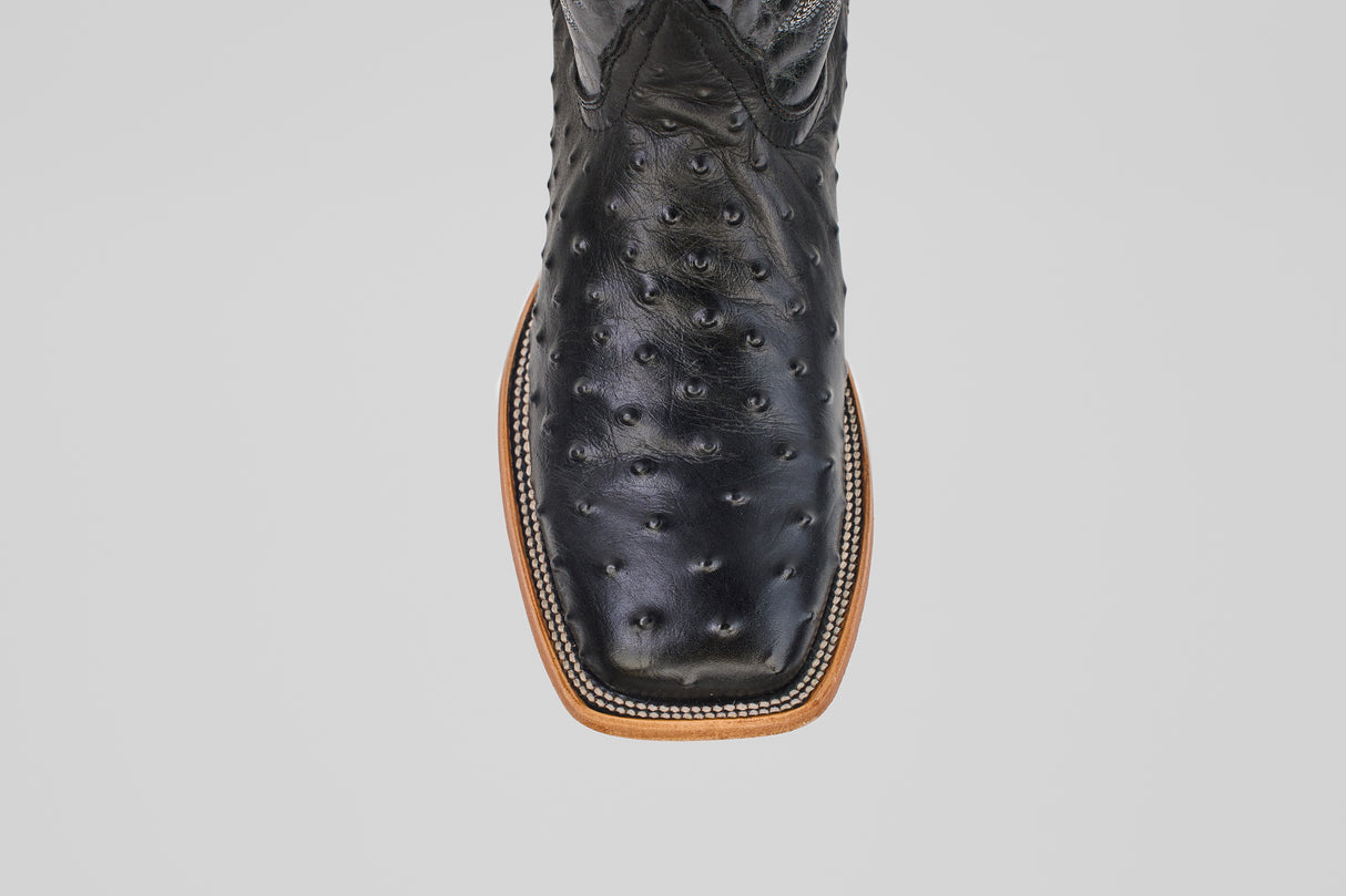 A close-up top view of the Ostrich Black - Embossed Leather - Square Toe (E424) boots with a light brown stitched sole, displayed on a plain gray background.
