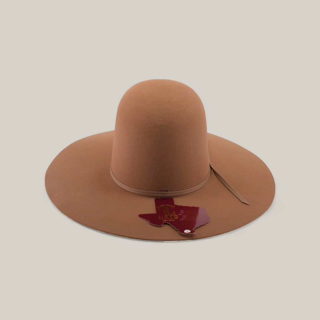 The 4X - Fawn - TC Hats is a wide-brimmed, light brown Western hat with a shapeable crown, shown on a plain background and featuring a Texas-shaped red tag attached to the brim.
