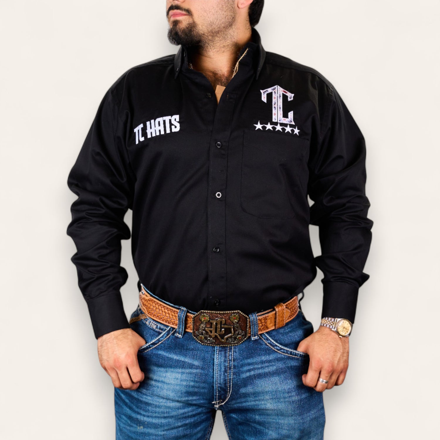 A man wearing the TC Hats - Black Red Aztec shirt, blue jeans, a brown belt with a large buckle, and a gold watch poses with his hands in his pockets against a plain background.