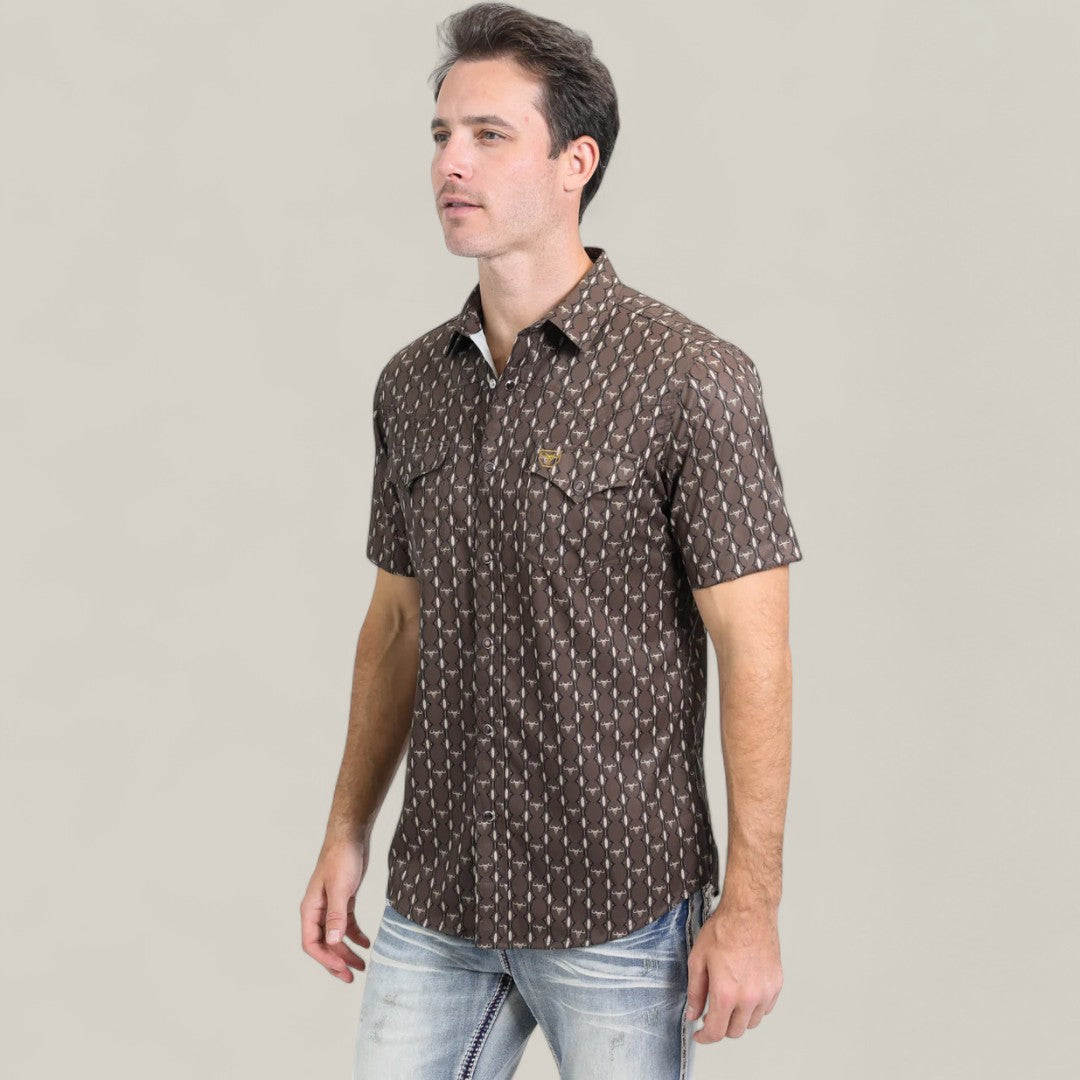 A man wearing the Mens Performance Western Short Sleeve Aztec Print Brown Shirt (PGW10643) and light blue jeans stands against a plain light gray background.