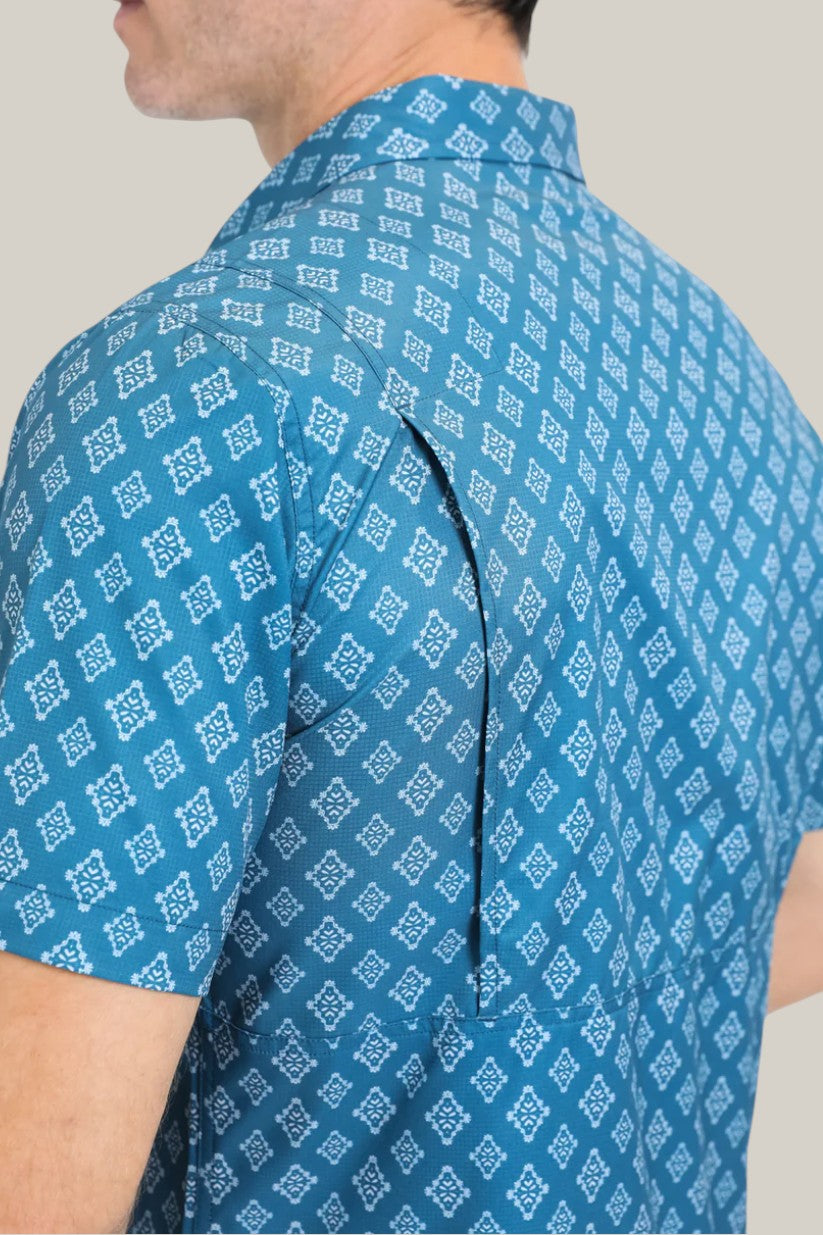 A man wears the Mens Performance Western Short Sleeve Aztec Print Blue Shirt (PGW10632), featuring a white geometric pattern, a hidden underarm zipper for ventilation, and moisture-wicking fabric for comfort.