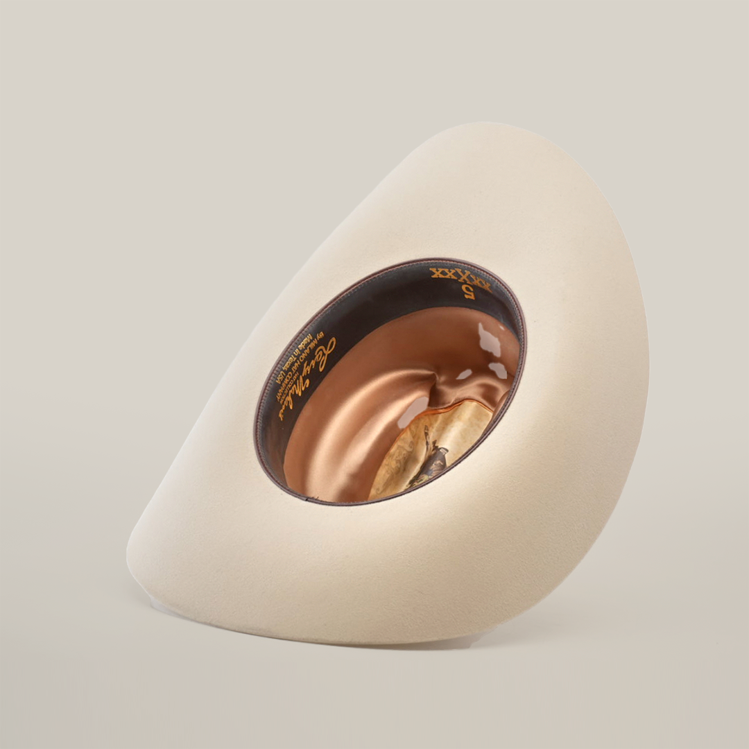 The 5X Dorado Belly, a beige wide-brimmed western hat, lies on its side to reveal a brown interior with gold Larry Mahan 5X text. Crafted from fur felt, it rests elegantly against a plain light background.
