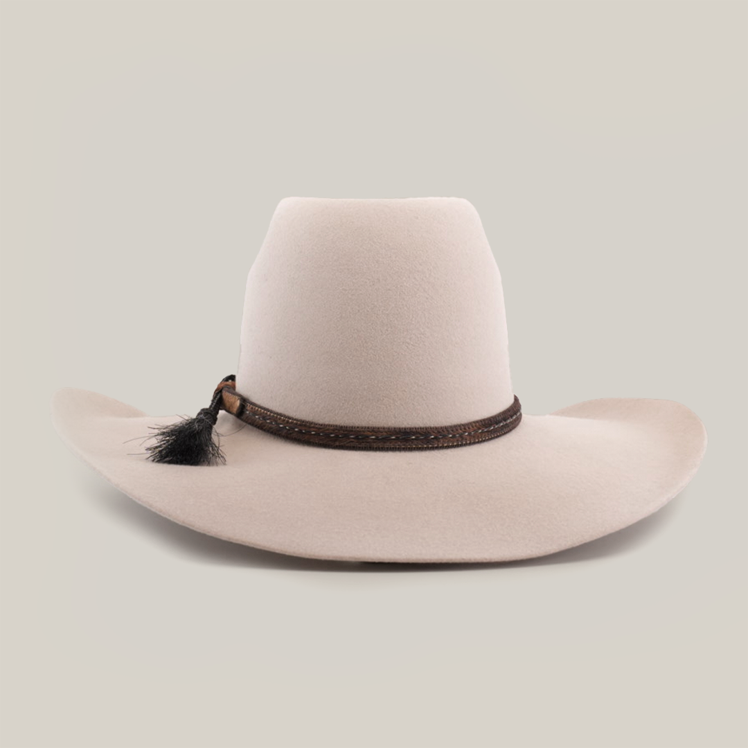 The 6X Brazil Belly is a beige wide-brimmed hat made from genuine sheep wool, featuring a tall crown and enhanced with a premium leather band with woven details and a small black feather.