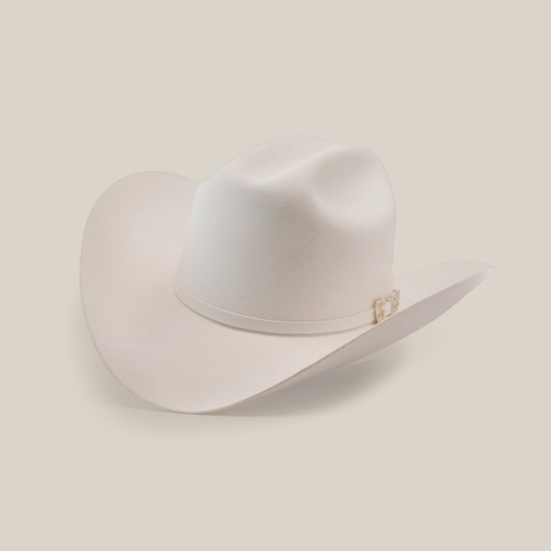 The 10X Jerarca White is a beige cowboy hat made from fine fur felt, featuring a wide brim and a decorative band around the crown. This classic western headwear, reminiscent of Larry Mahan 10X style, is presented against a plain white background.