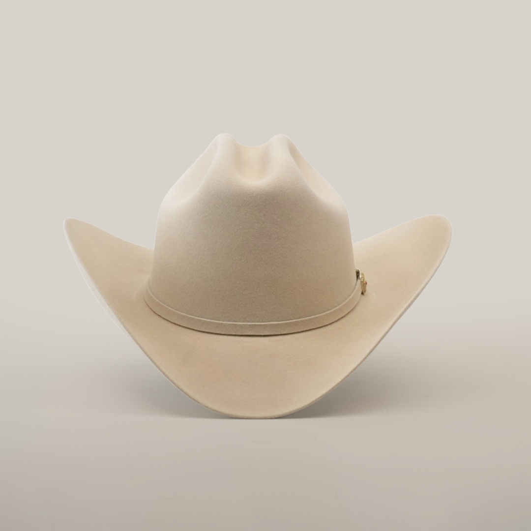 The 6X Real Belly, a premium beige fur cowboy hat, sports a wide brim and pinched crown with subtle decorative stitching, set against a plain white background.