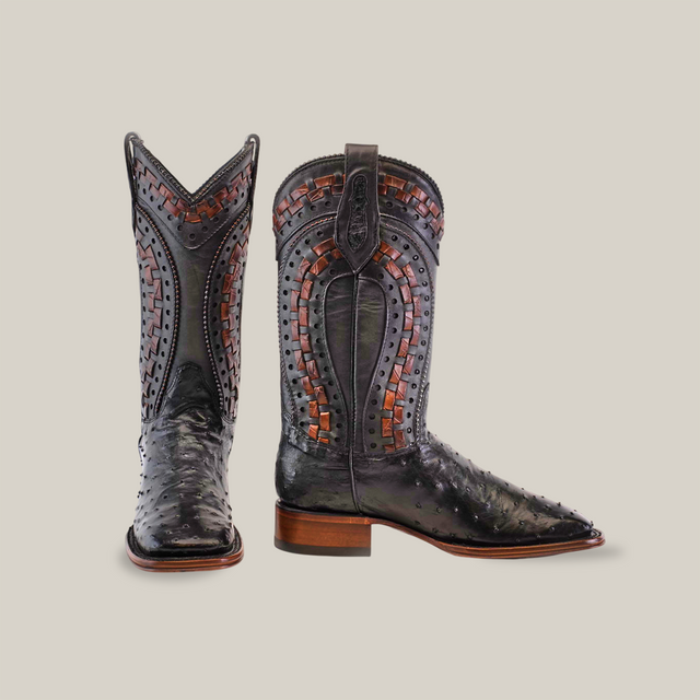 The Exotic Karoo Ostrich - Herradura boots in black feature intricate woven designs and detailed stitching. With a Western flair, they showcase ostrich leather from the Platinum Collection, offering a striking look with one boot forward and the other to the side.