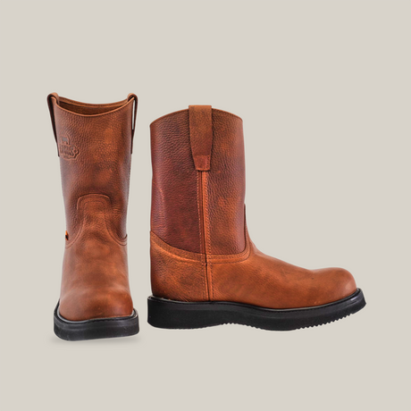 A pair of Brandy Roper - Tractor Sole - Composite Toe work boots, crafted from premium cowhide leather with brown uppers. One boot is upright, the other tilts forward displaying its logo. Pull straps on the sides complete this display of handcrafted excellence.