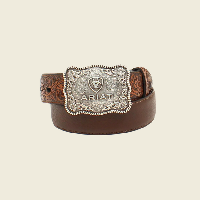 The Ariat Boys Belt Flower Tooled Brown - A1301002 is a brown leather belt with floral embossing, featuring a large rectangular silver buckle engraved with patterns and the ARIAT logo, making it a standout Western-inspired accessory.