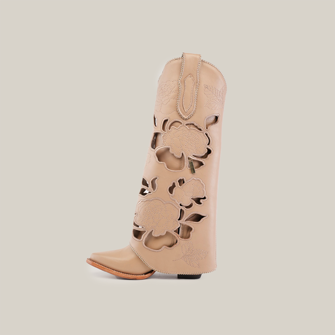 The Roma Flowers Tall Shaft Cream - J Toe is a beige cowboy boot with intricate floral cutouts, leather soles, a pointed toe, and a low heel. It features an inner dark lining and is set against a plain white background.