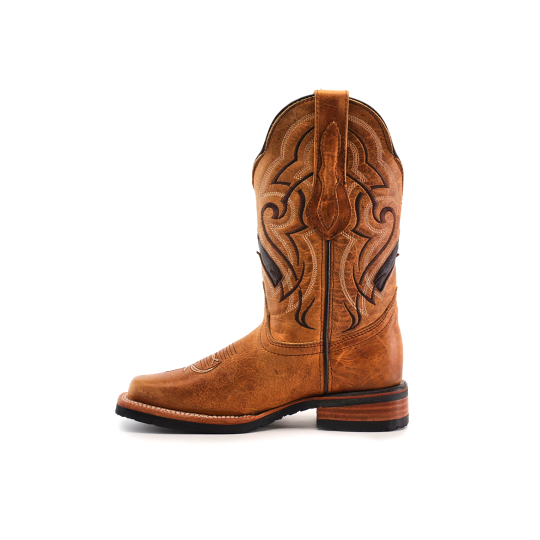 The Wild Mustard Slip Resistant Sole Rodeo Toe boot features a tan cowhide leather design with intricate shaft stitching, a rounded toe, and low stacked heel. It includes pull loops at the top for easy access and offers a slip-resistant sole for stability. Displayed on a white background.