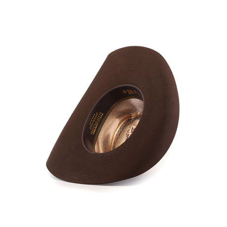 The 6X Bull Brown, a luxury felt hat with a wide asymmetric brim, is showcased against a white background. Its label, adorned with decorative patterns, emphasizes the hats distinctive shape and texture.