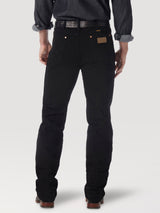 A person faces away from the camera, wearing a dark long-sleeve shirt with rolled-up sleeves, black Wrangler Cowboy Cut Slim Fit Jeans - 0936WBK made from premium denim, and brown leather shoes. A belt is partially visible above the waistband of their jeans.