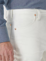 Someone wearing the Wrangler Cowboy Cut Slim Fit Jean - 0936WHI, in a blue shirt, highlights the jeans waistband and pocket details, with their hand showcasing the classic Wrangler patch.