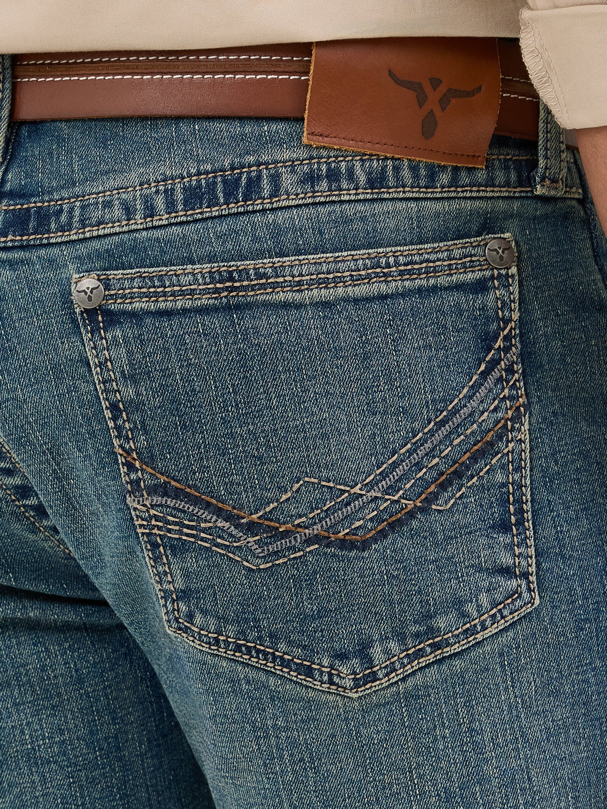 Close-up of the Wrangler Mens 20X Extreme Relaxed Fit Jeans - 1044MWXMA shows a back pocket with decorative stitching, brown leather belt at the waist, and a branded leather patch. These premium denim jeans boast a slightly faded look, offering relaxed fit and ultimate comfort.