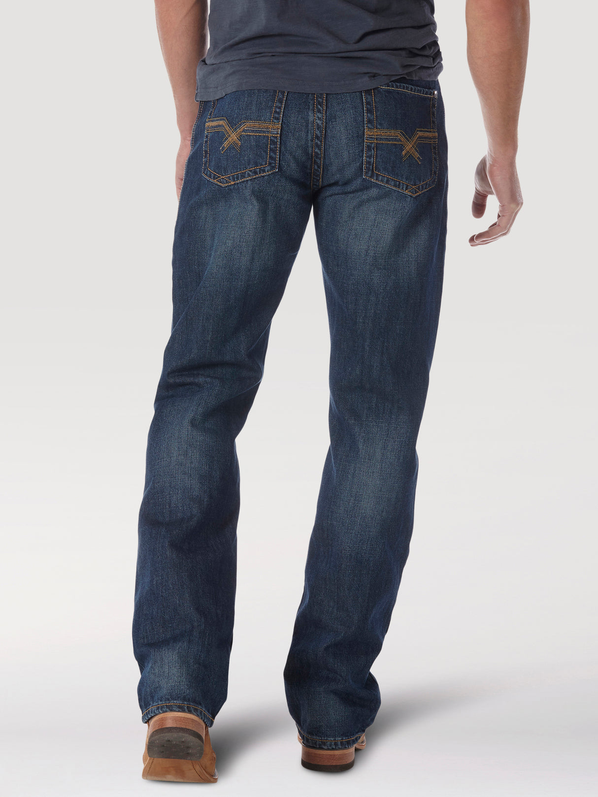 A person, seen from behind, wears Wrangler® 20X® No. 33 Relaxed Straight Leg jeans in dark blue with decorative back pocket stitching, paired with a dark T-shirt and brown shoes against a plain white background.