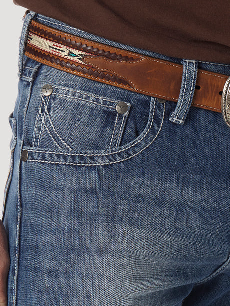 Close-up of a person wearing Mens Wrangler 20X No. 42 Vintage Bootcut Jeans - 1042MWXLB in premium denim with detailed stitching, paired with a decorative brown leather belt and partially visible metal buckle against a light, neutral background.