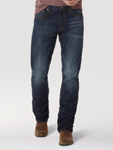 A person is standing in Wrangler® 20X® No. 42 - Vintage Boot Jean 1042MWXRD, which are dark blue with a thigh-faded design, paired with brown leather boots. Their hands are out of frame or in pockets.