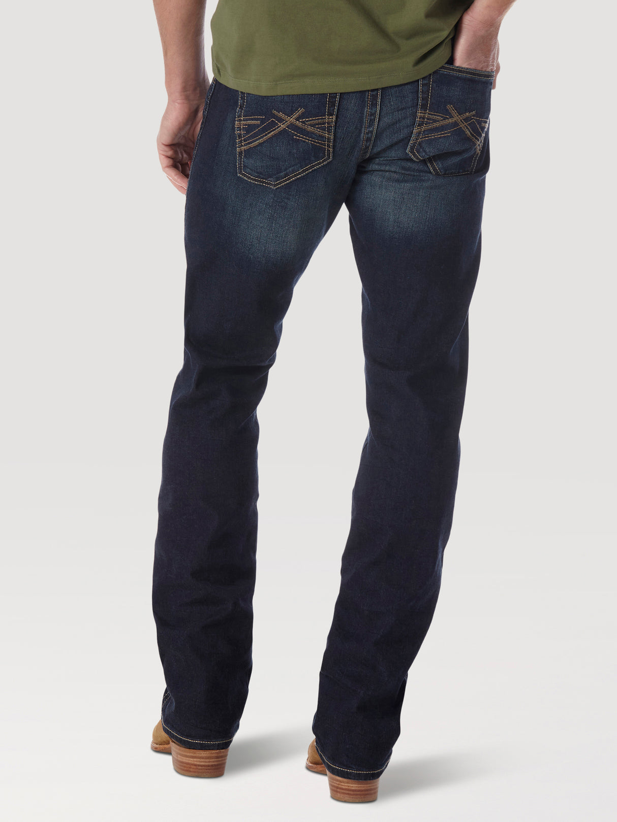 A person is shown from the back wearing Mens Wrangler 20X No. 42 Vintage Bootcut Jeans (42MWXRD) with decorative stitching on the back pockets, paired with a green shirt and brown shoes against a plain background.