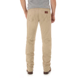 A person stands with their back to the camera, wearing a gray shirt and Mens Wrangler Retro Slim Fit Straight Leg Pant - 1088MWZFN in beige, noted for its visible pocket stitching and leather tag. Brown shoes complete the relaxed fit look.