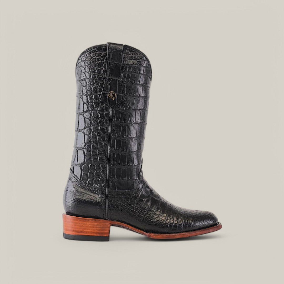 The Exotic Full American Alligator Black Round Toe boot features premium alligator leather with a textured pattern, a brown stacked heel, and a wooden sole, displayed on a light beige background.