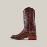 A side view of the luxurious Exotic Full American Alligator boot in brown, featuring a rounded toe and low wooden heel. The intricate texture reminiscent of alligator leather stands out as the boot is displayed upright against a plain, neutral background.