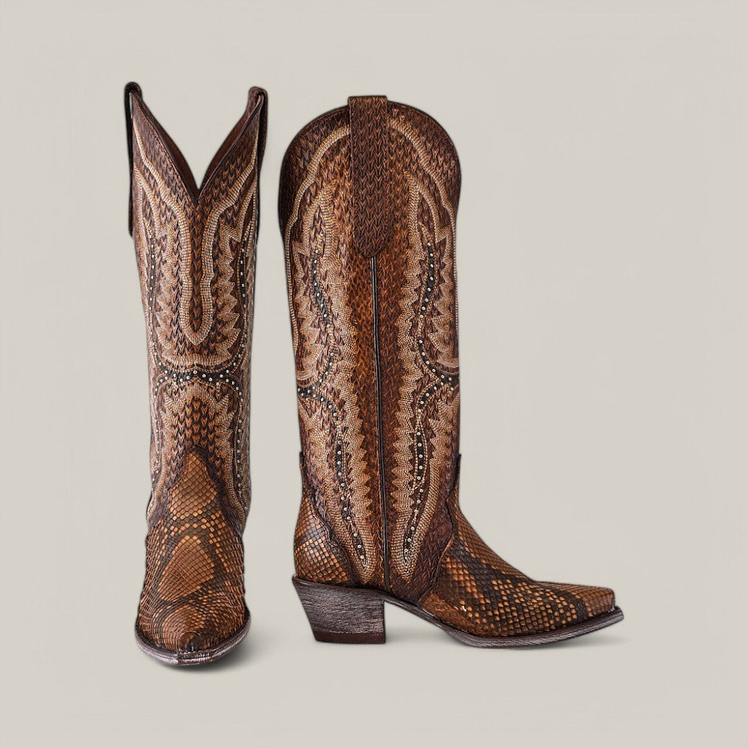 The Athala Exotic Python Tamarindo features intricate stitching and a premium python pattern on brown leather. With a snip toe and stacked heel, these boots stand tall against a light gray backdrop, embodying Western heritage.