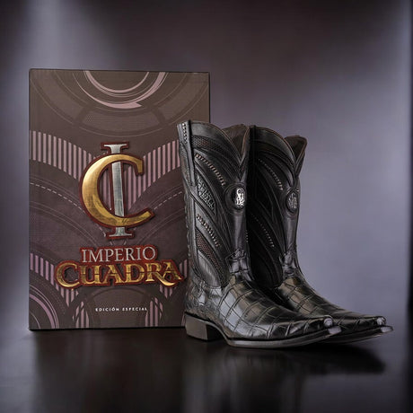 A pair of Alligator Belly Black cowboy boots with a narrow square toe and intricate detailing is placed beside a large box. The box features the text Imperio Cuadra Edición Especial and showcases a stylized C logo, emphasizing the exclusivity of these special Cuadra Boots.